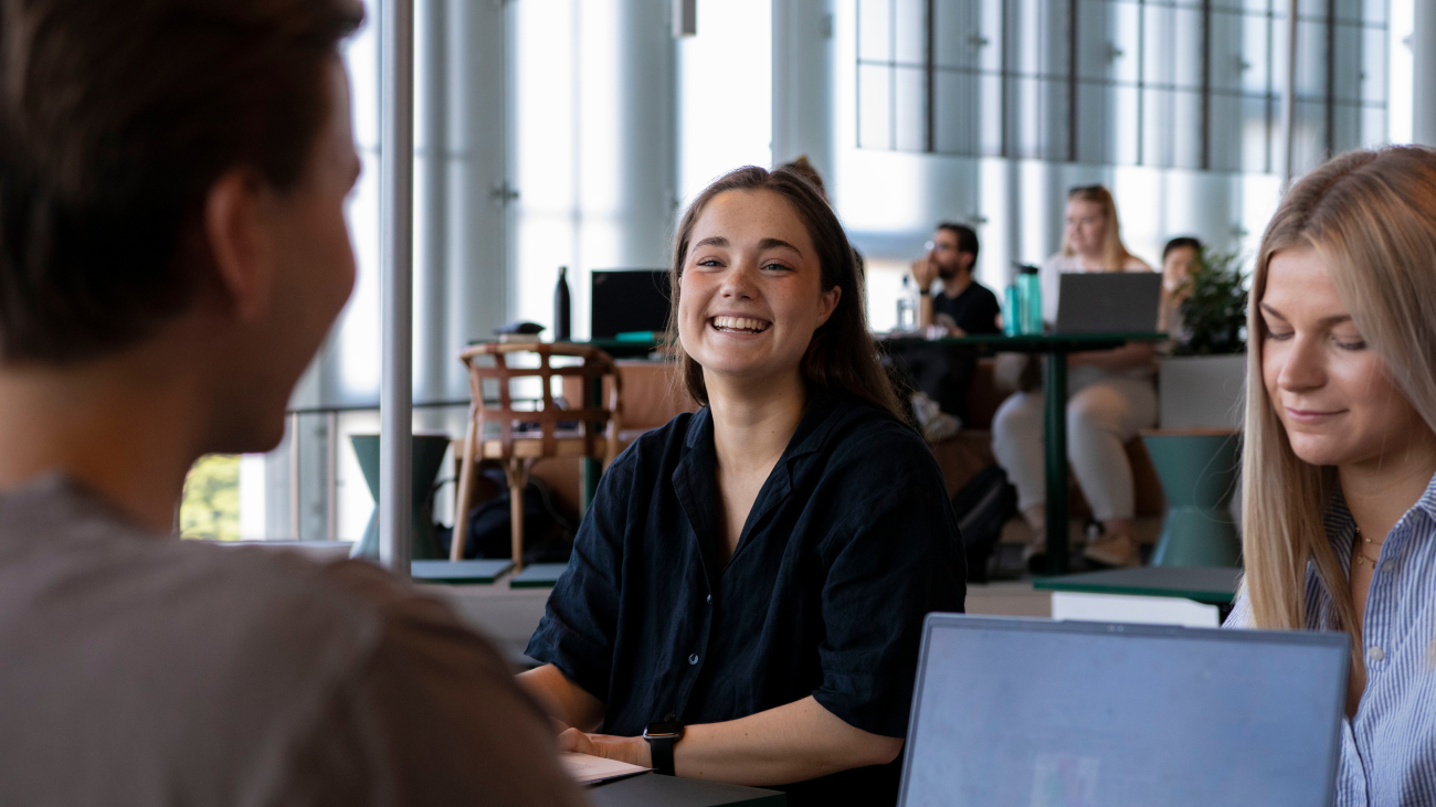 Smilende studenter som sitter rundt et bord på campus.