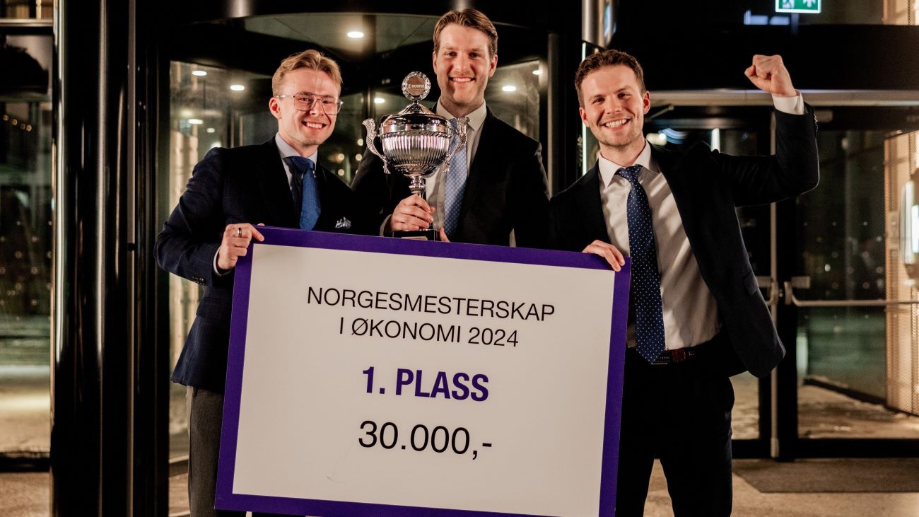 Tre unge menn som holder en pokal og en sjekk og feirer at de nettopp har vunnet NM i økonomi 2024.